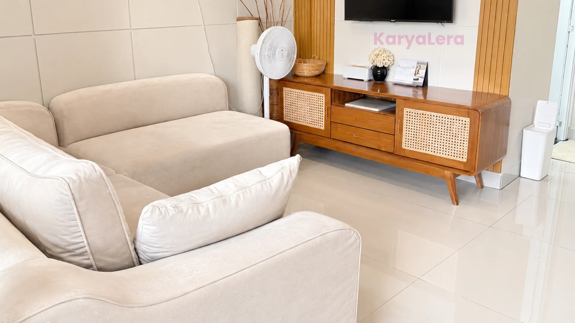 Ruang keluarga dengan sofa krem, kabinet kayu berpintu rotan, dan TV dinding