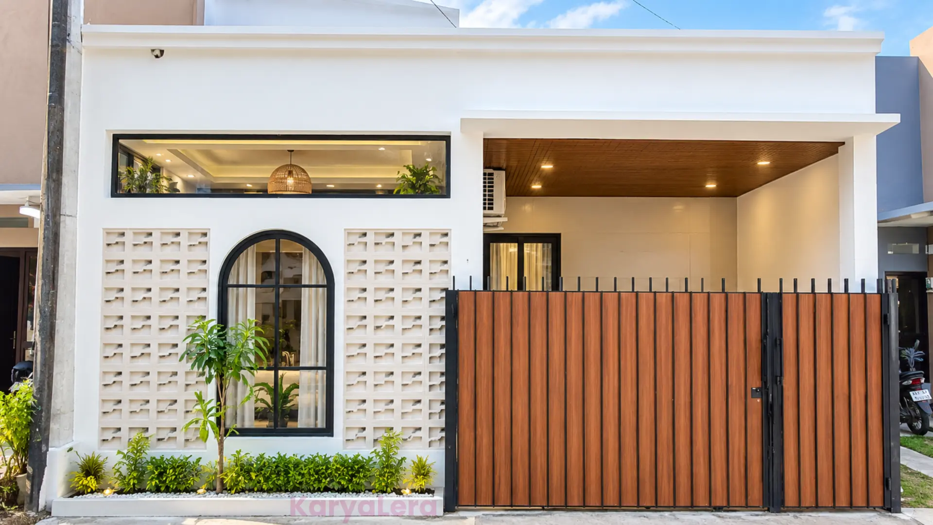 Fasad rumah minimalis KaryaLera dengan pagar kayu, roster putih, dan carport berplafon kayu